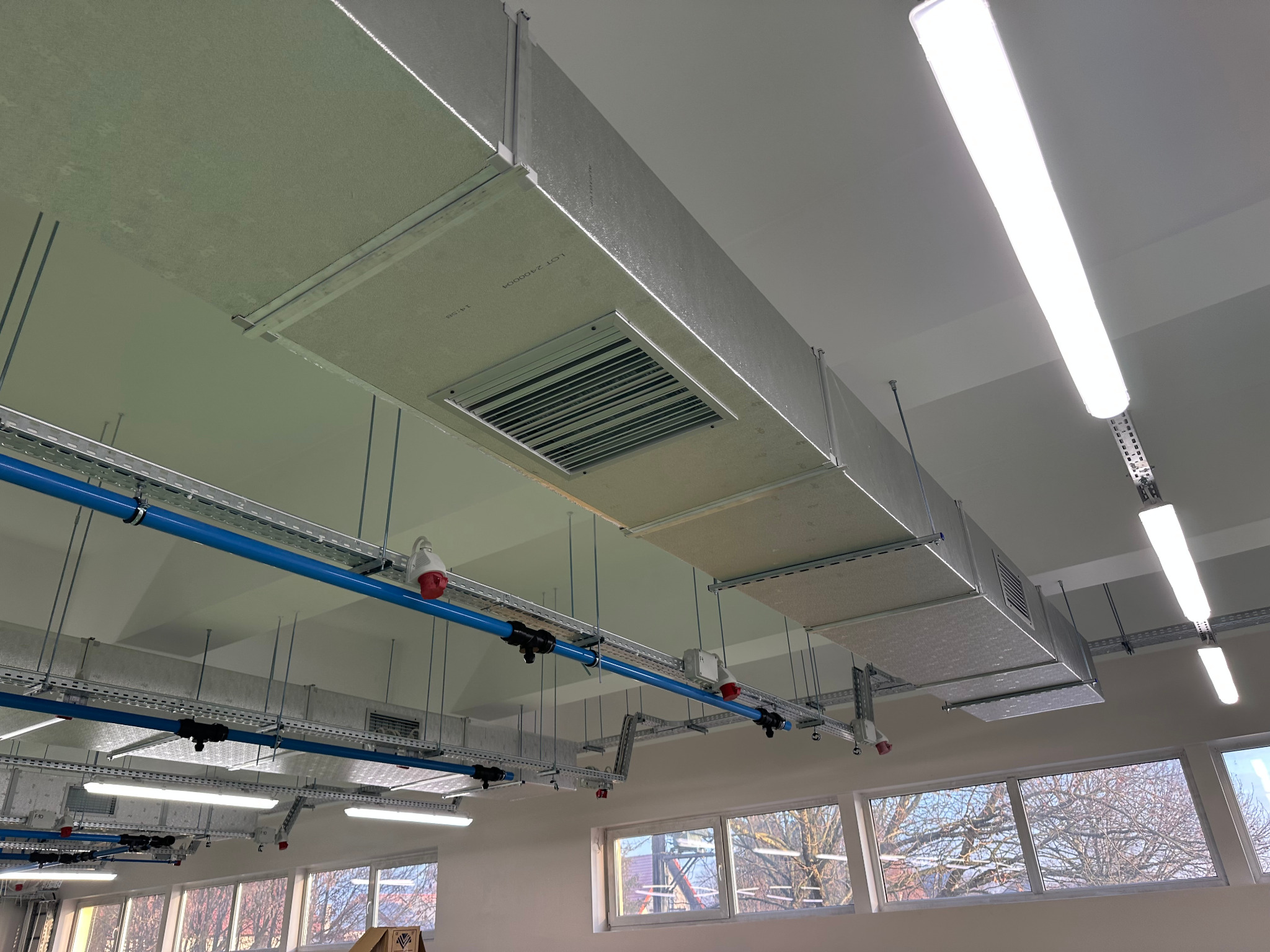 Kompleksowa instalacja wentylacji mechanicznej z izolowanymi kanałami PIR, widoczna pod sufitem, z elementami regulacji temperatury nawiewu i oświetleniem LED.