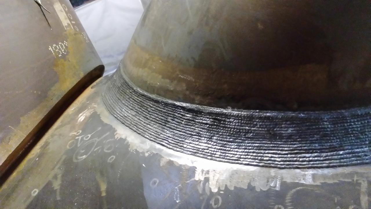 Spoina na rurze o dużej średnicy, widoczne ślady spawania wielowarstwowego, oznaczenia na powierzchni rury.