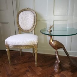 WOODFINISH - Stylowe krzesło z tapicerką w panterkę i stolik z podstawą w kształcie ptaka na parkiecie ułożonym we wzór jodełki, na tle panelowej ściany.