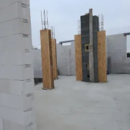 Wznoszenie ścian domu z betonu komórkowego, widoczne zbrojenia pionowe w szalunkach z płyt OSB, elementy konstrukcyjne w surowym stanie.