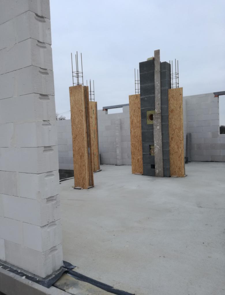 Wznoszenie ścian domu z betonu komórkowego, widoczne zbrojenia pionowe w szalunkach z płyt OSB, elementy konstrukcyjne w surowym stanie.