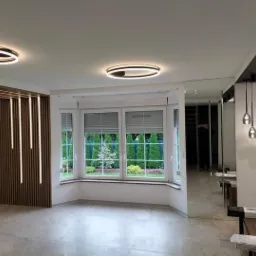 Nowoczesne wnętrze z oknem wykuszowym, drewnianą ścianką z oświetleniem LED i lustrzaną ścianą, uzupełnione okrągłymi lampami sufitowymi.