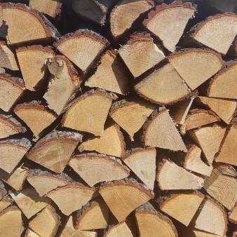 Równomiernie ułożone, pocięte kawałki drewna opałowego z widoczną korą na krawędziach, oświetlone naturalnym światłem.
