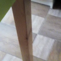 Fragment podłogi z paneli imitujących drewno, z widoczną nogą stołu i fragmentem zielonego obrusu. Panele ułożone w szachownicę z odcieni beżu i szarości.