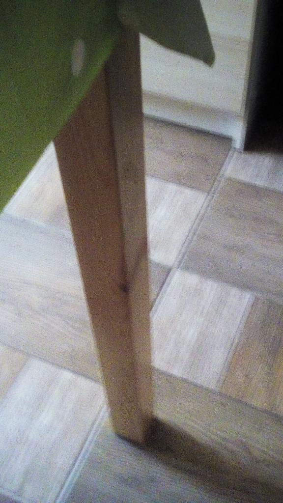 Fragment podłogi z paneli imitujących drewno, z widoczną nogą stołu i fragmentem zielonego obrusu. Panele ułożone w szachownicę z odcieni beżu i szarości.