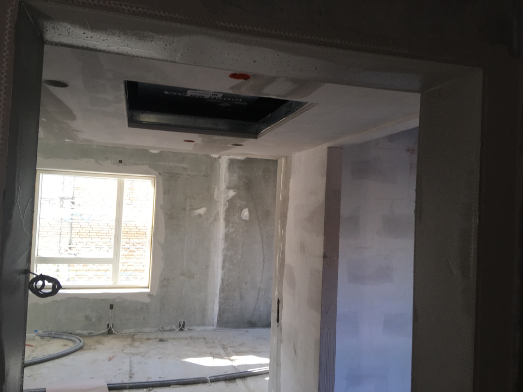 Wnętrze w trakcie prac wykończeniowych: ściany po nałożeniu gładzi, widoczne przewody elektryczne, otwór w suficie pod instalację.