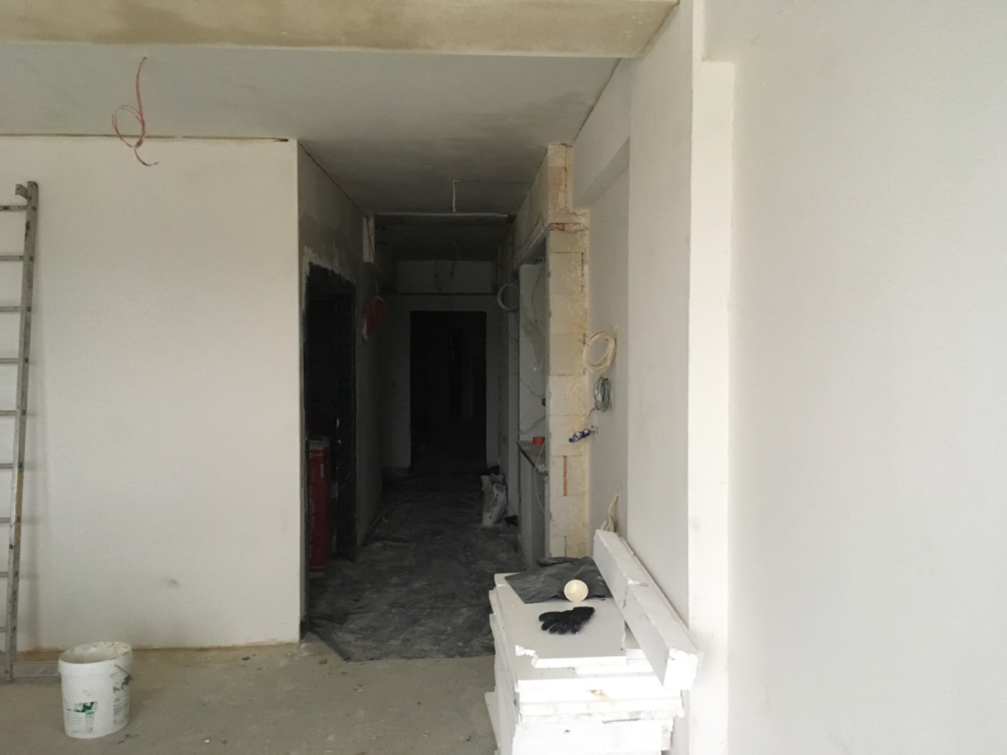Wnętrze w trakcie remontu w Dąbrowie Górniczej: widok na korytarz z surowymi ścianami, częściowo nałożona gładź, widoczna drabina, wiadro z zaprawą i materiały budowlane.
