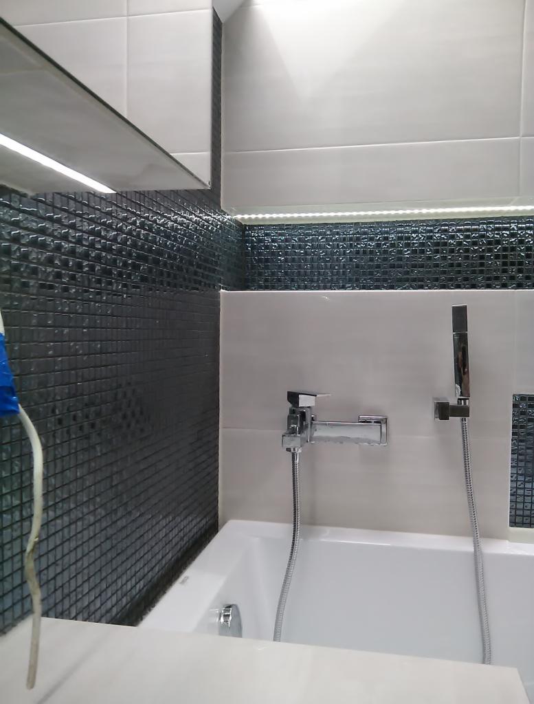 Nowoczesna łazienka w Radomiu z czarno-białymi płytkami mozaikowymi, podświetleniem LED i chromowaną armaturą nad białą wanną.