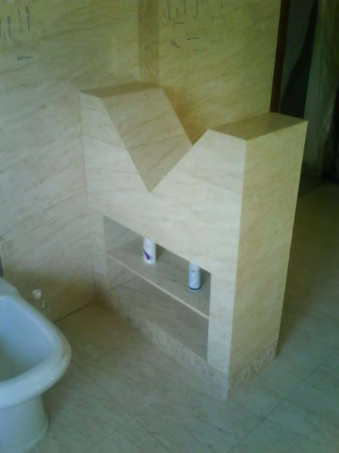 Beżowa marmurowa zabudowa umywalki z półką i bidetem w łazience, widoczne kosmetyki na półce.