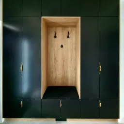 Czarna zabudowa meblowa z drewnianą wnęką z siedziskiem i wieszakami, uchwyty w kolorze złotym.