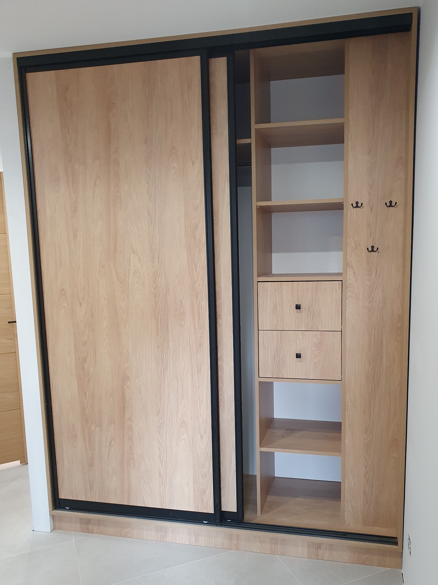 Jasna szafa przesuwna z czarnymi obramowaniami, z otwartą częścią z półkami, szufladami i wieszakami na ubrania, widok z bliska.