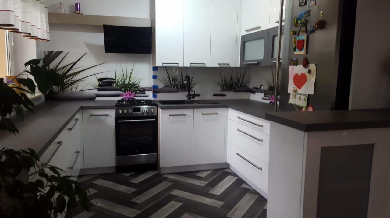 Nowoczesna kuchnia z białymi szafkami, ciemnym blatem, wzorzystą podłogą, roślinami i dekoracyjnym panelem ściennym z motywem zen.