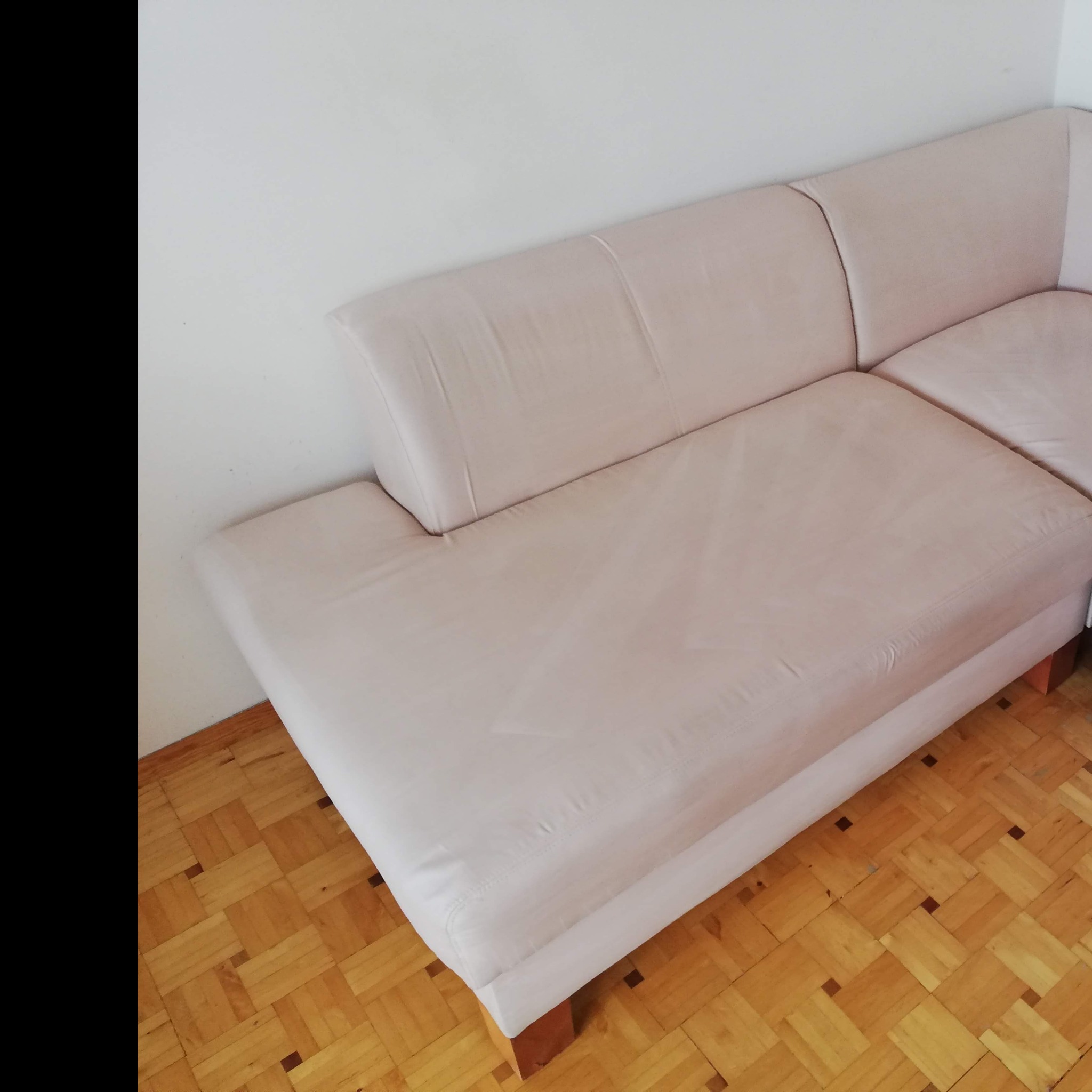 Jasna, narożna kanapa ze skórzanym obiciem, ustawiona na parkiecie. Widok z góry, ukazujący fakturę materiału i wzór podłogi.