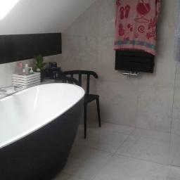 DIMAX SPÓŁKA Z OGRANICZONĄ ODPOWIEDZIALNOŚCIĄ - Nowoczesna łazienka na poddaszu z wolnostojącą wanną na tle szarych płytek, czarnego grzejnika i minimalistycznego krzesła.