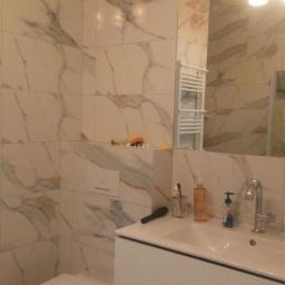 DIMAX SPÓŁKA Z OGRANICZONĄ ODPOWIEDZIALNOŚCIĄ - Nowoczesna łazienka w Bełchatowie z białymi płytkami imitującymi marmur, podwieszana toaleta, biała szafka pod umywalką i dekoracyjne lampy wiszące.