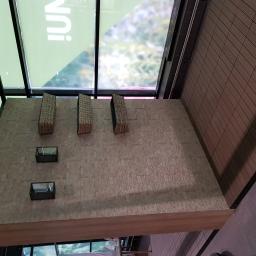 DIMAX SPÓŁKA Z OGRANICZONĄ ODPOWIEDZIALNOŚCIĄ - Elewacja budynku z jasnej, nieregularnej kostki, z trzema wystającymi elementami dekoracyjnymi i dwoma niewielkimi oknami w ciemnych ramach, widok z dołu w kierunku przeszklonego dachu.