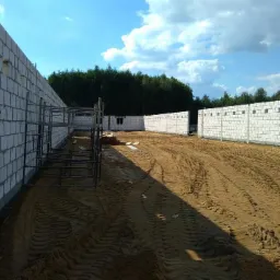 Budowa hali usługowej w trakcie wznoszenia ścian z bloczków betonowych, widoczne rusztowania i przygotowany teren pod wylewkę.