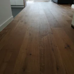 Ułożona, ciemna, lakierowana podłoga z desek z widocznymi słojami drewna, perspektywa od progu w stronę sofy.