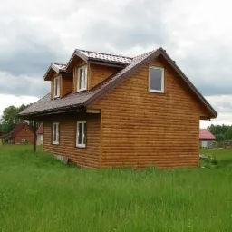 Nowoczesny, parterowy dom z brązową elewacją w Harrow, otoczony wysoką trawą i innymi budynkami w tle.