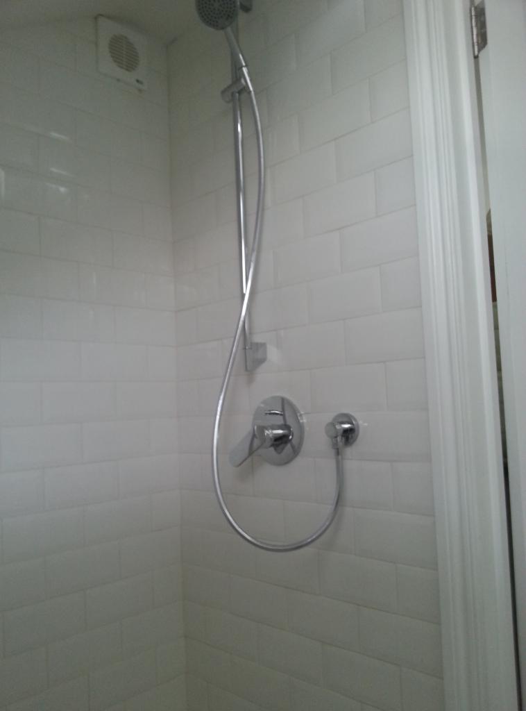 Nowoczesna kabina prysznicowa z białą, ceglaną okładziną ścienną, chromowaną baterią i deszczownicą.