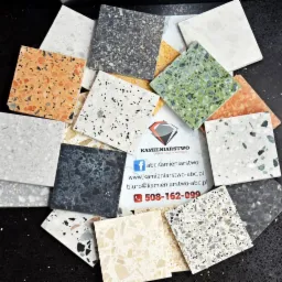Prezentacja próbek kwadratowych płyt z konglomeratu o różnorodnej kolorystyce i fakturze, ułożonych wokół wizytówki firmy kamieniarskiej.
