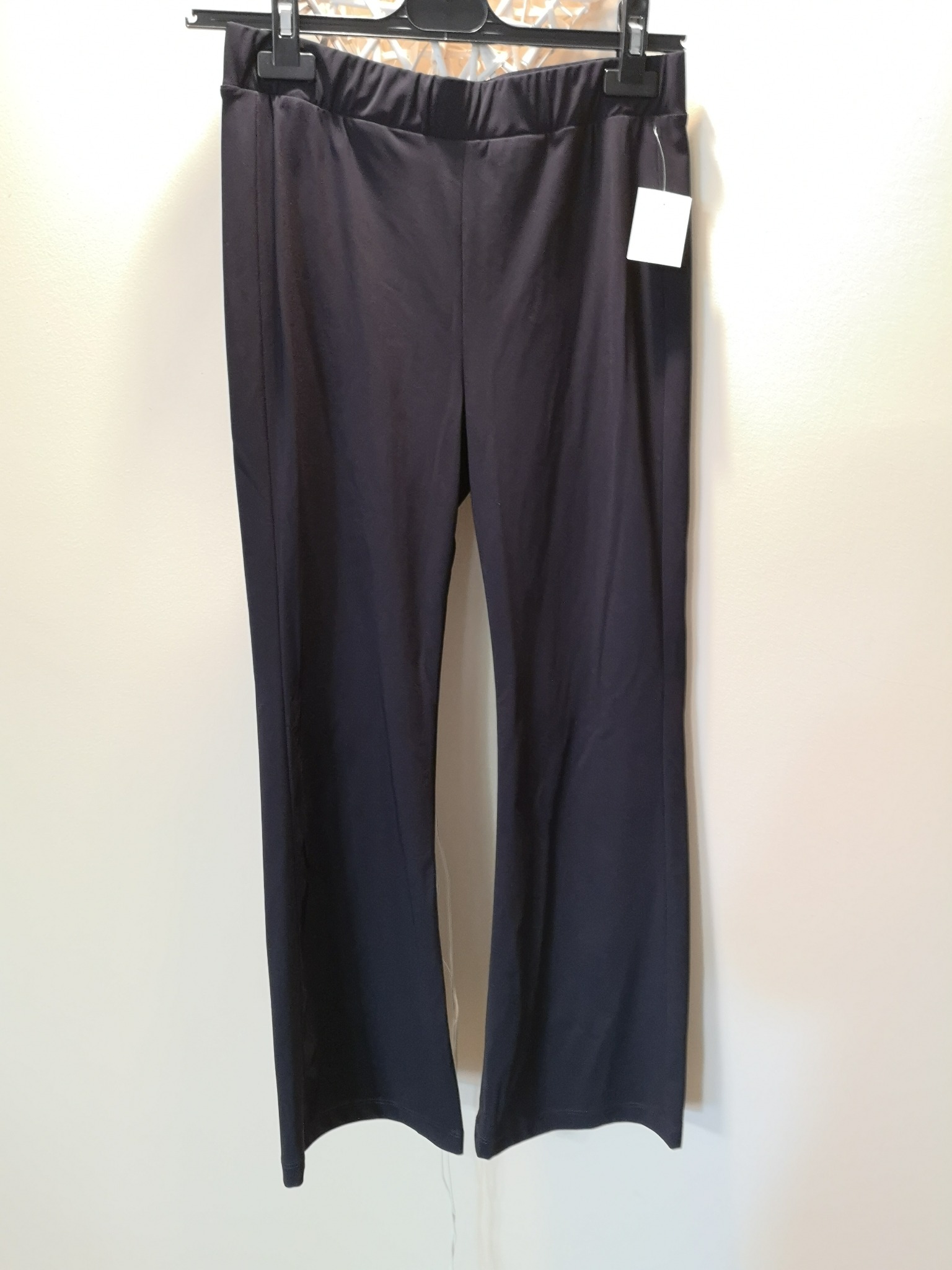 Ciemne, damskie spodnie dresowe z metką, wiszące na wieszaku na tle jasnej ściany, oferowane w Nowym Tomyślu.