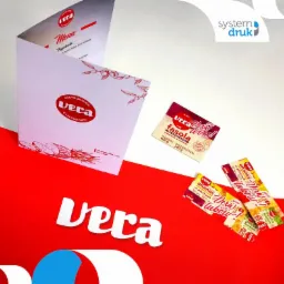 Rozłożona karta menu restauracji Vera obok opakowań produkt&oacute;w spożywczych z logo Vera na czerwono-białym tle, z widocznym logo drukarni System Druk.