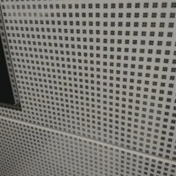 Wz&oacute;r na ścianie z regularnie rozmieszczonymi czarnymi rozetami na białym tle, widoczne łączenia płyt