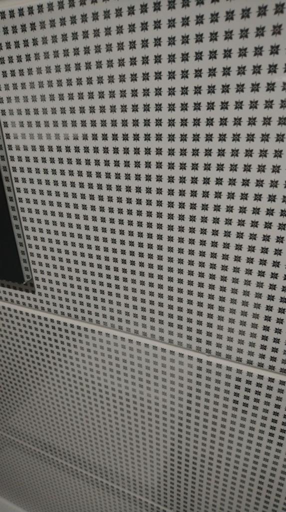 Wzór na ścianie z regularnie rozmieszczonymi czarnymi rozetami na białym tle, widoczne łączenia płyt