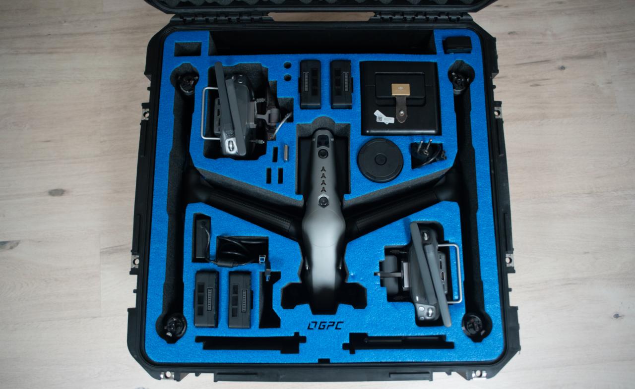Dron w czarnej walizce z niebieskim wypełnieniem, widoczne akcesoria i baterie, logo DGPC.