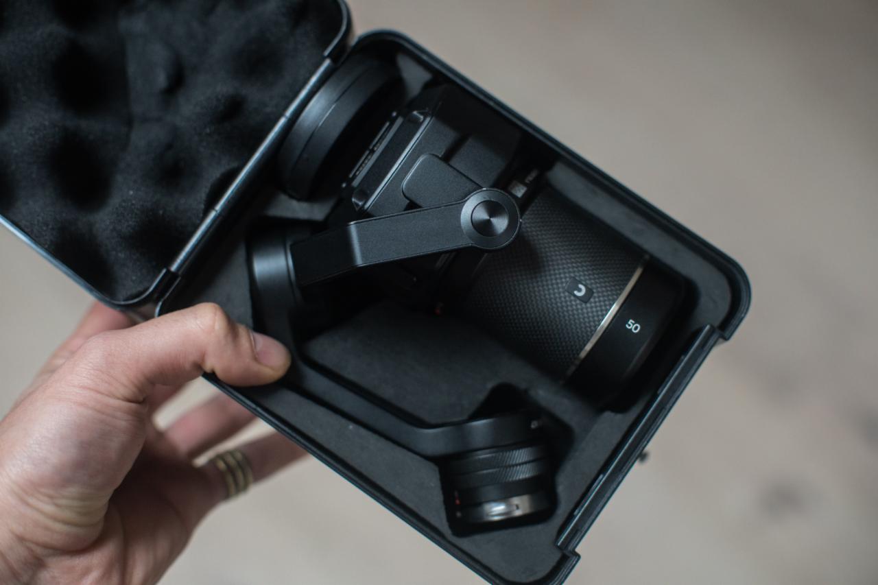 Czarny stabilizator kamery z obiektywem 50mm, umieszczony w czarnym, wyściełanym futerale, trzymany w dłoni z widocznymi pierścionkami.