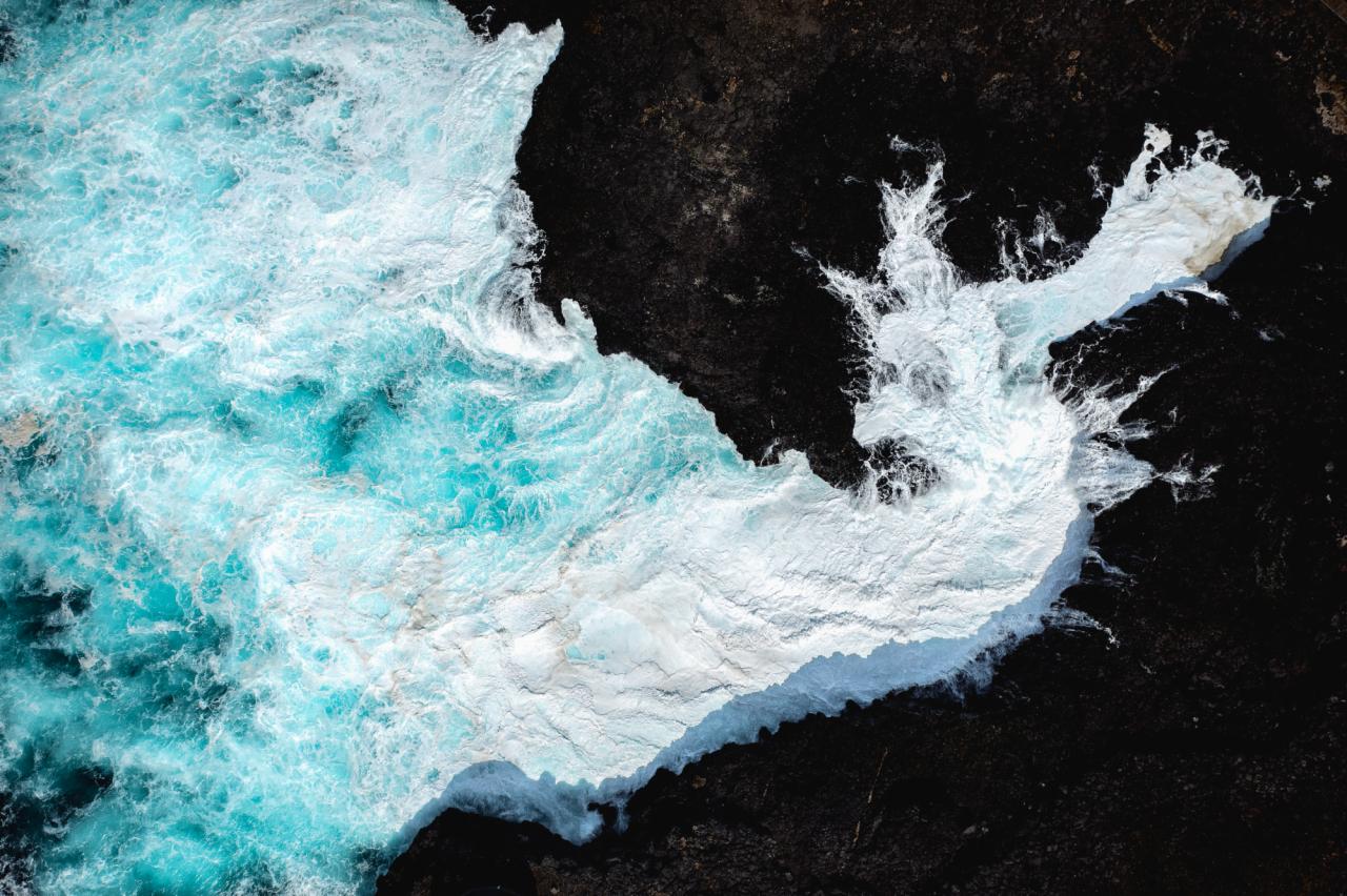 Turkusowa woda rzeki spływająca po ciemnych skałach, uchwycona z lotu ptaka.