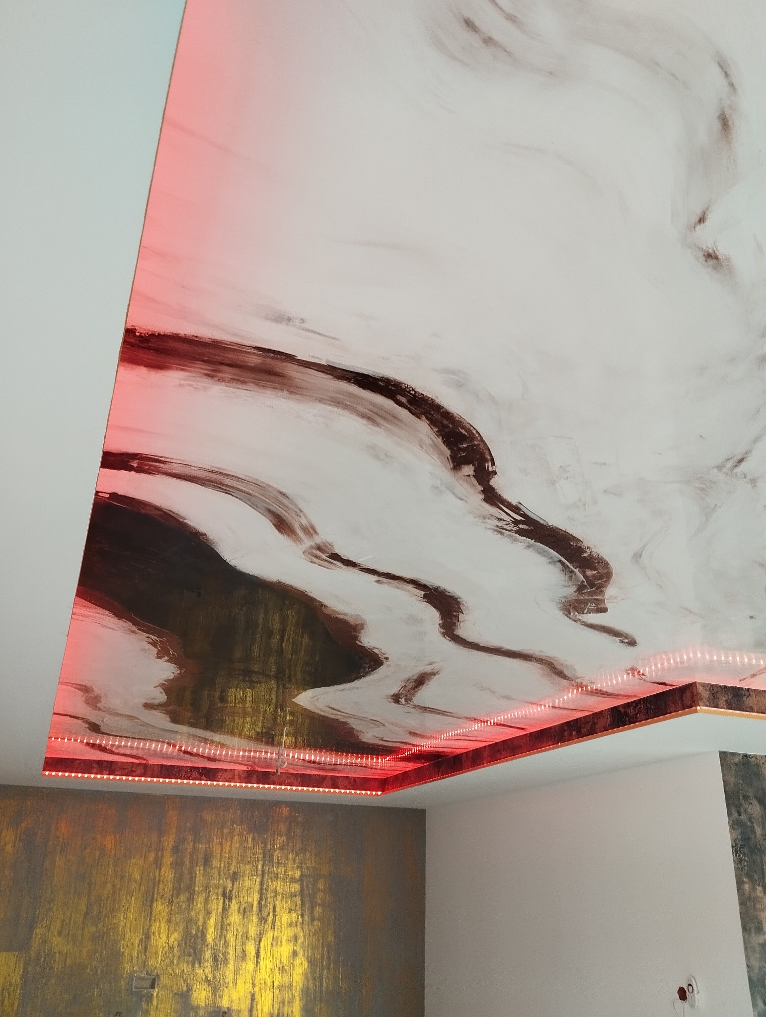 Podwieszany sufit z płyty karton-gips, imitujący marmur, podświetlony czerwoną listwą LED, widok od dołu.