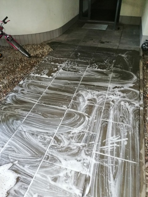 Czyszczenie kostki brukowej przed wejściem do budynku, widoczne ślady piany po umyciu pod ciśnieniem.