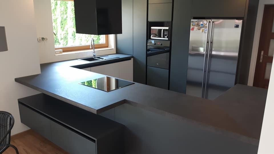 Nowoczesna kuchnia w odcieniach szarości z blatem roboczym w kształcie litery L, z wbudowaną płytą indukcyjną i oknem z widokiem na zieleń.