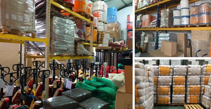 Magazyn z paletami i wózkami widłowymi, na półkach składowane różne materiały, niektóre owinięte folią stretch.