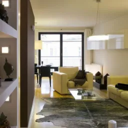 Jasne, nowoczesne wnętrze salonu z drewnianą podłogą, beżowymi meblami, szklanym stolikiem kawowym i dekoracyjną ścianą w odcieniach brązu.