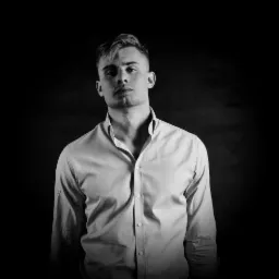 Portret młodego mężczyzny w rozpiętej koszuli na ciemnym, teksturowanym tle, czarno-biały, oświetlenie studyjne.