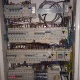 Rozdzielnica elektryczna z licznymi zabezpieczeniami nadprądowymi i różnicowoprądowymi, widoczne przewody wewnątrz obudowy.