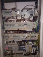 Rozdzielnica elektryczna z licznymi zabezpieczeniami nadprądowymi i różnicowoprądowymi, widoczne przewody wewnątrz obudowy.