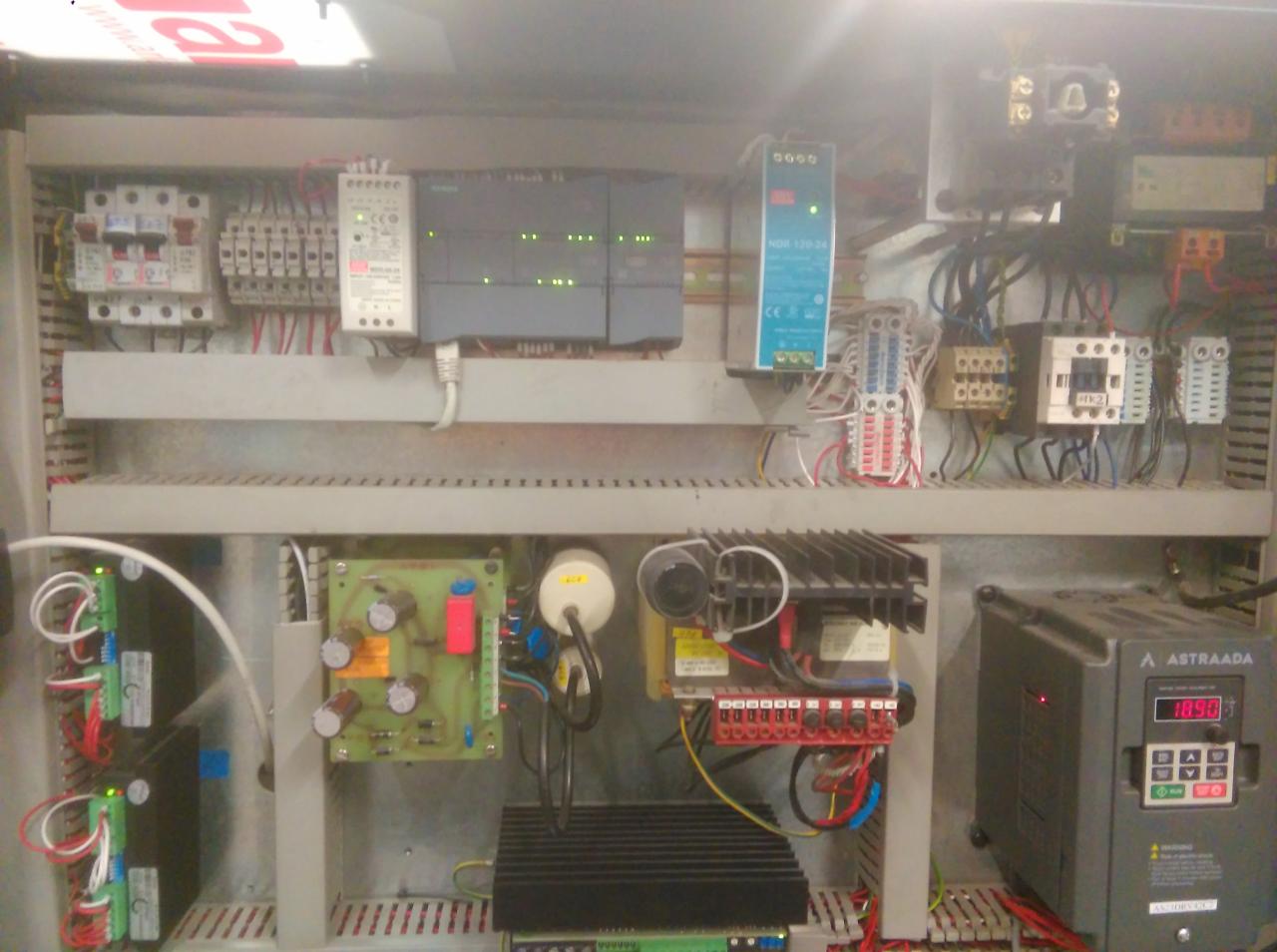 Wnętrze szafy sterowniczej z widocznymi elementami automatyki, w tym sterownikami PLC Siemens, zasilaczem NDR 120-24, stycznikami i przetwornicą częstotliwości Astraada, okablowanie i elementy...