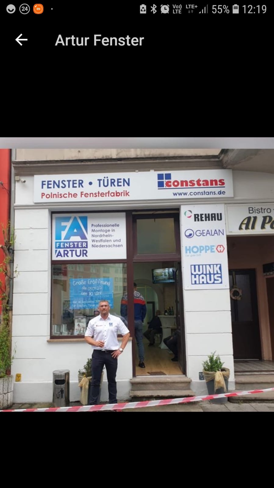 Fasada firmy Artur Fenster, polskiego producenta okien i drzwi, z właścicielem pozującym przed wejściem, na witrynie widoczne logo firmy oraz informacje o ofercie i producenci profili.