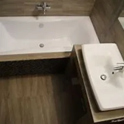 Nowoczesna łazienka z białą wanną obudowaną mozaiką i prostokątną umywalką nablatową, drewnopodobne płytki na podłodze i ścianach, chromowana armatura.