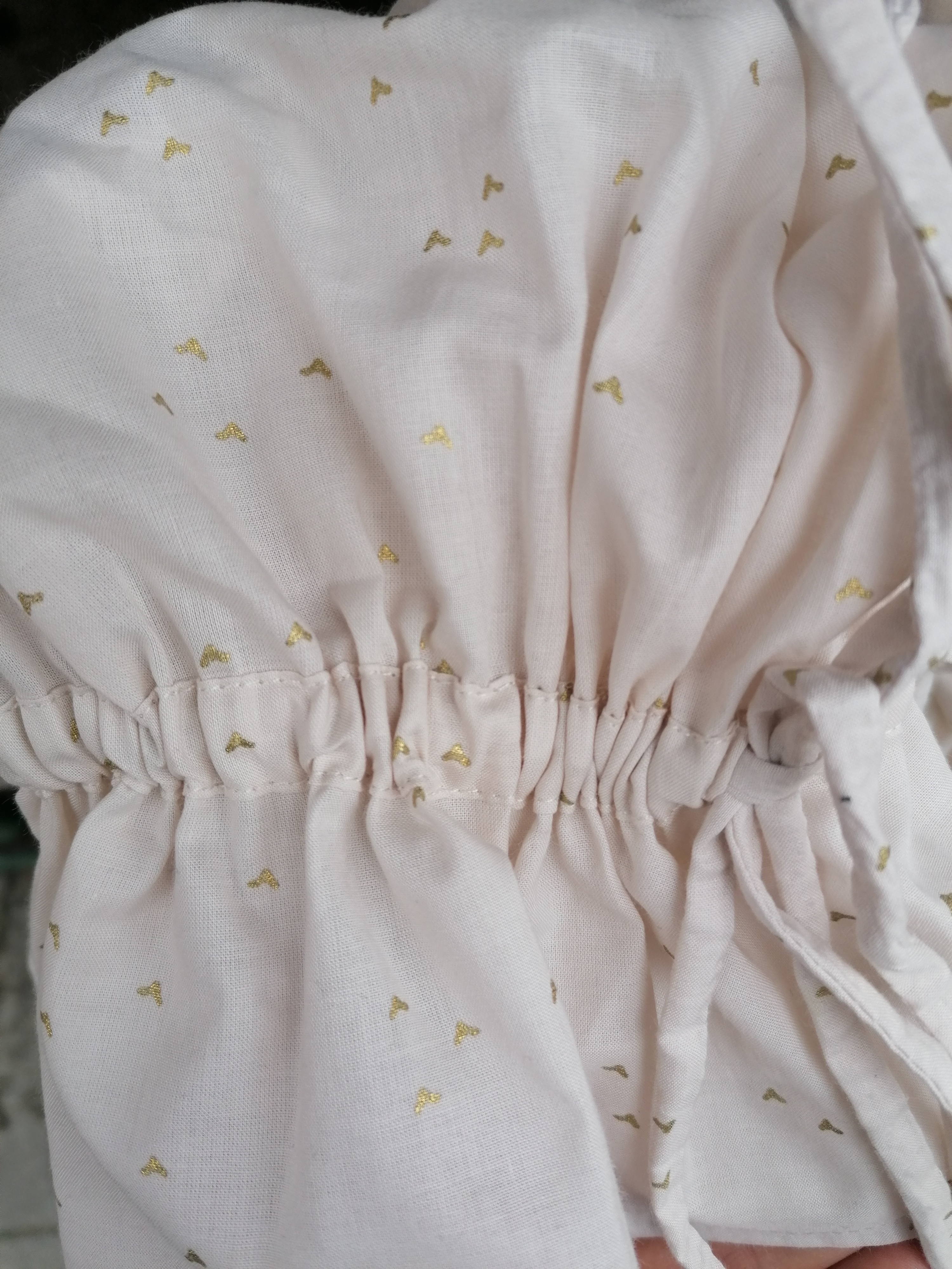 Detale marszczenia i wiązania w jasnej, wzorzystej tkaninie z drobnymi, złotymi motywami w kształcie litery T.