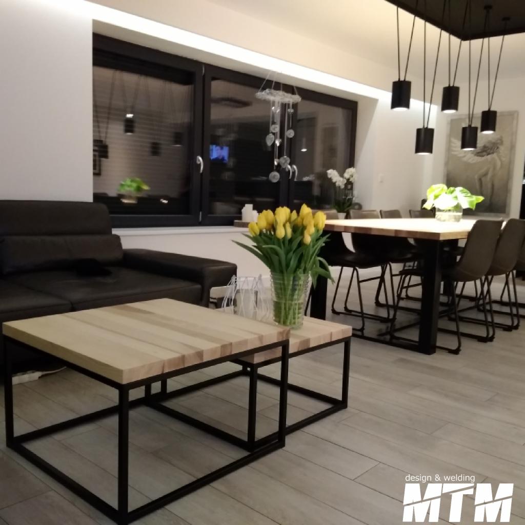 Dwa stoliki kawowe z jasnego drewna i czarnymi, metalowymi nogami w salonie w Lublińcu, z bukietem żółtych tulipanów i czarną skórzaną sofą w tle.