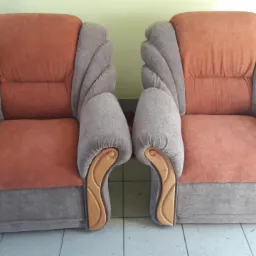 Dwa fotele tapicerowane w odcieniach pomarańczy i szarości, z dekoracyjnymi drewnianymi elementami na podłokietnikach, ustawione na kafelkach.