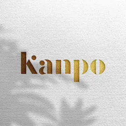 Złote logo 'Kanpo' wytłoczone na białym, teksturowanym tle z cieniem liści.