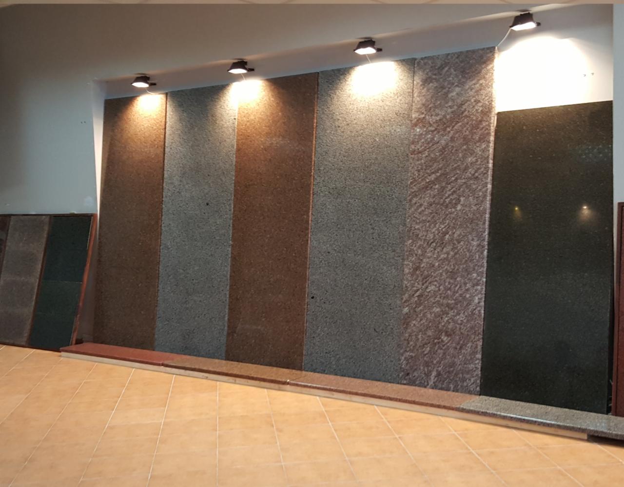 Ekspozycja różnych kolorów i faktur płyt kamiennych podświetlonych punktowymi lampami sufitowymi w jasnym pomieszczeniu.