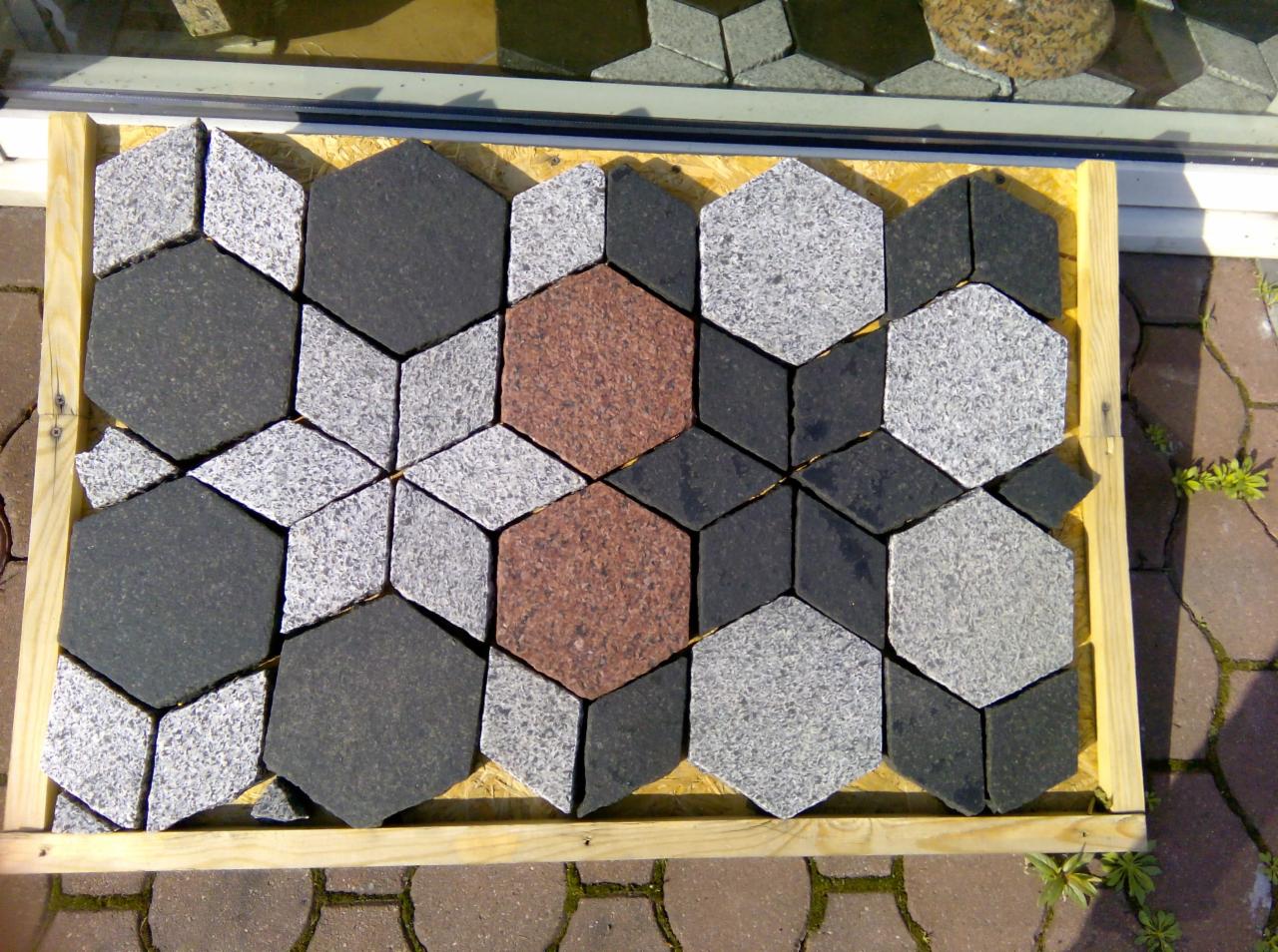 Ekspozycja kostki granitowej w drewnianej ramie: sześciokątne kostki w odcieniach szarości, grafitu i brązu, ułożone w geometryczny wzór.