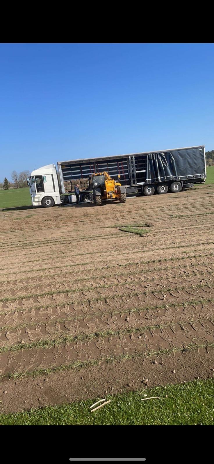 Rozładunek trawy z rolki z ciężarówki za pomocą wózka widłowego na przygotowanym polu. Widoczne ułożone fragmenty darni i świeże ślady opon.